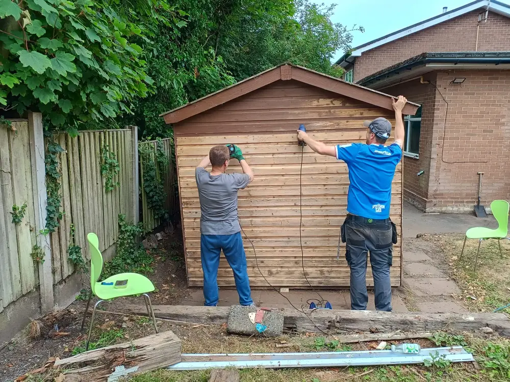 People sanding a shed, ready for paint